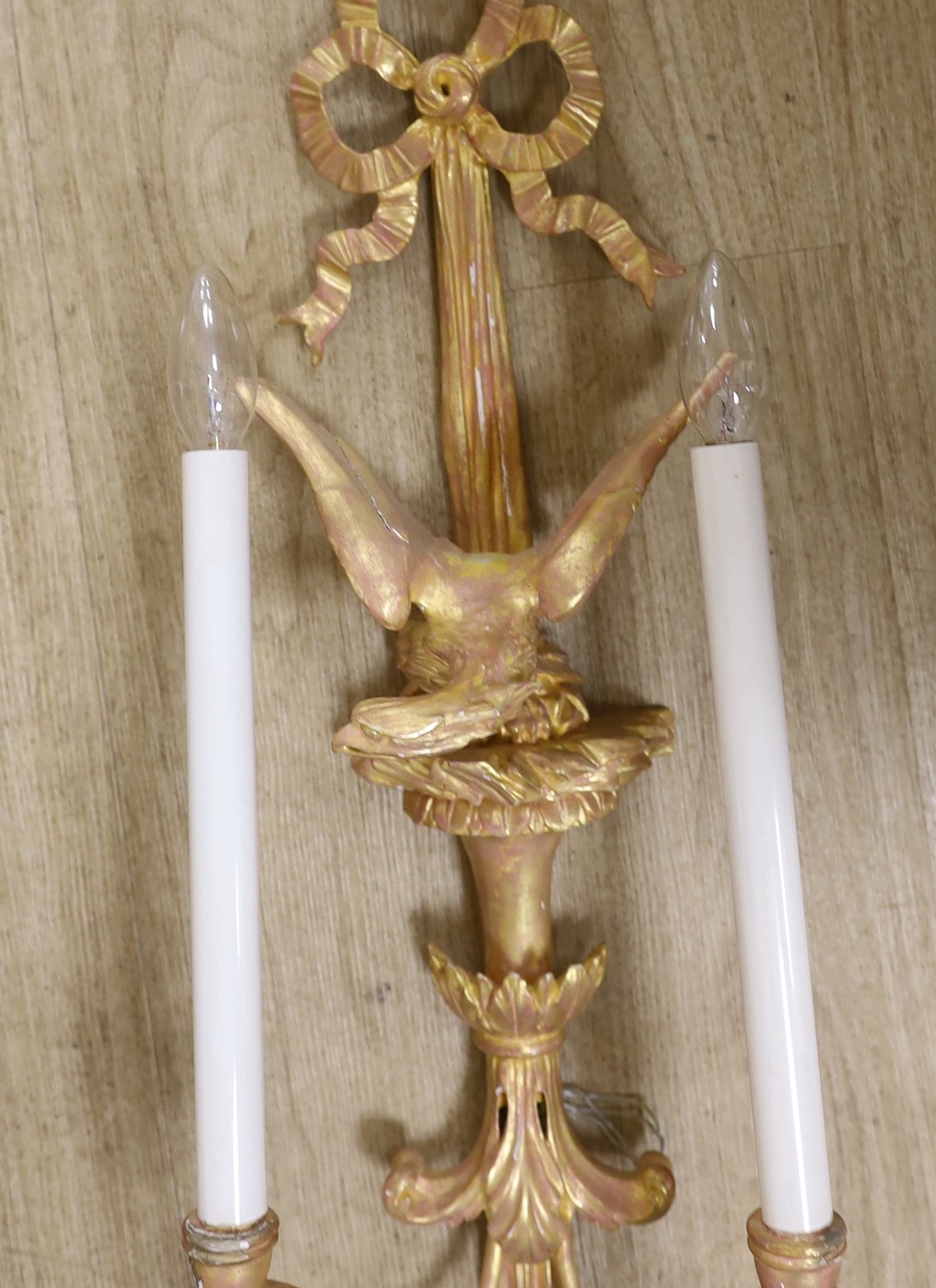 A pair of Louis XVI style carved giltwood wall lights, with ribbon crests and winged eagle stems, over tasselled bases, height 79cm